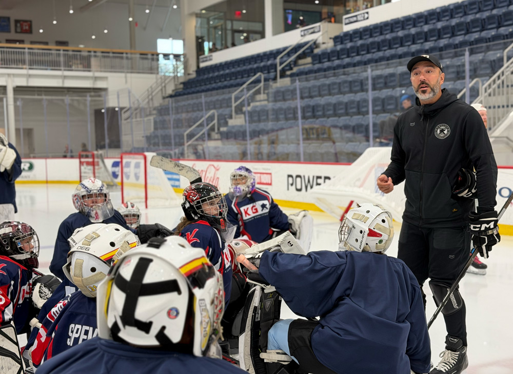 Coach addressing a group of youth goalies along the boards