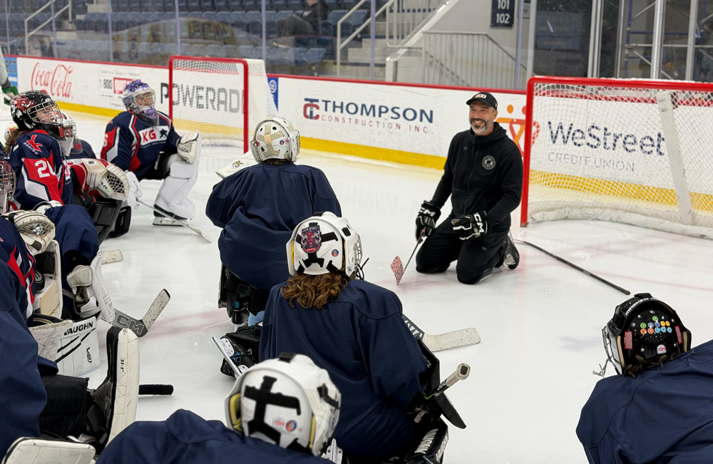 Coach kneeling with goalies gathered around the crease